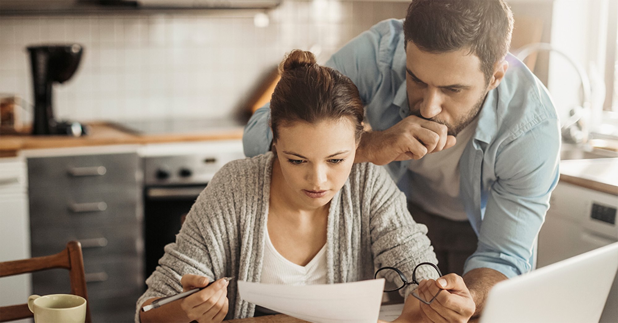A man and woman look over important documents in their kitchen.
