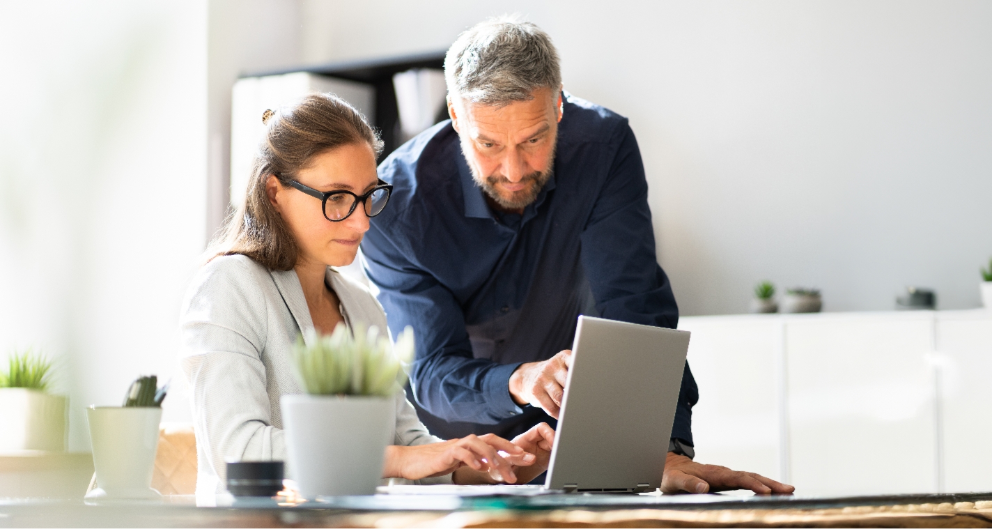 I a brightly lit clean office a man and woman work together intently on a laptop