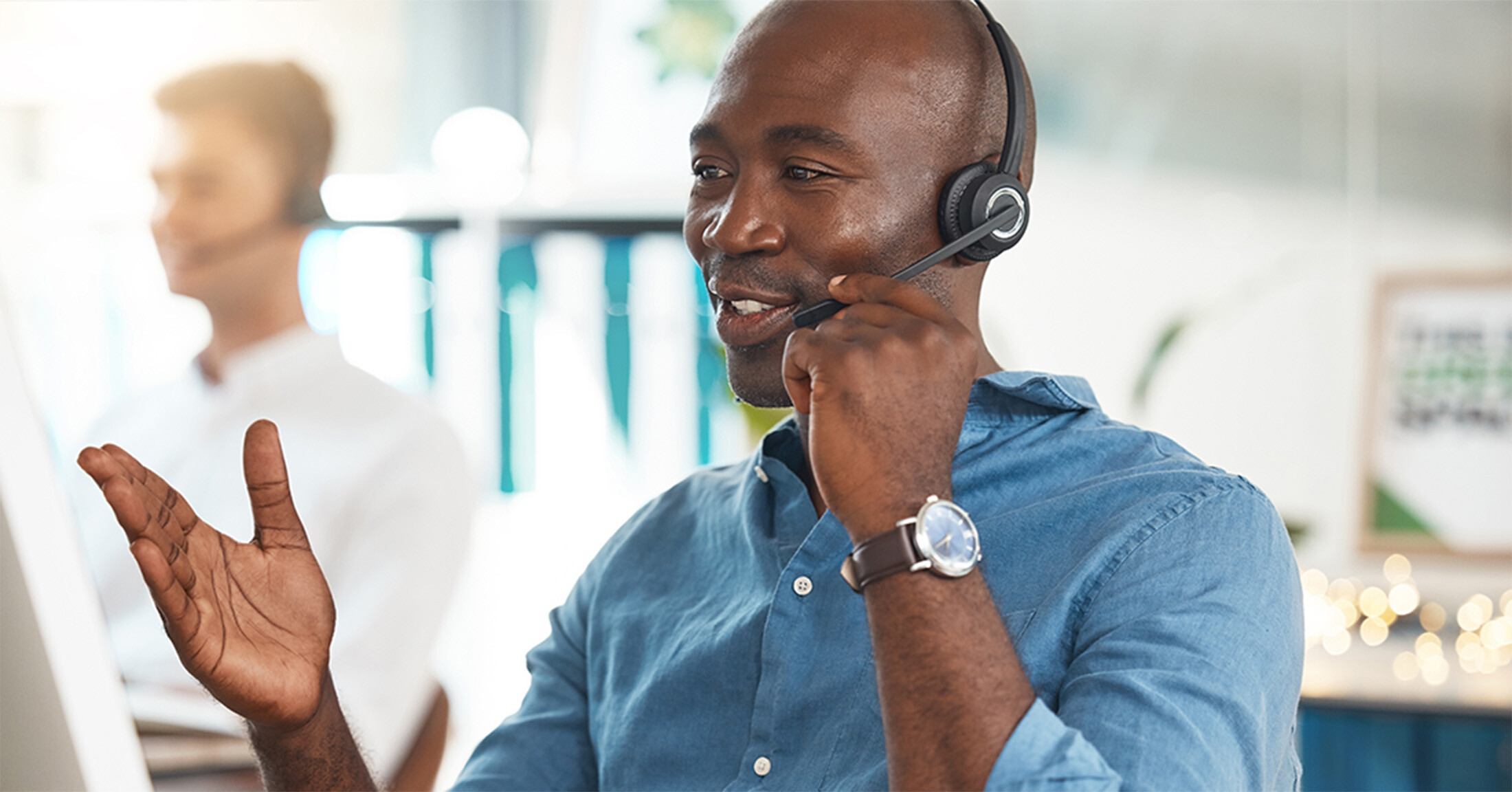 Man speaking to a customer with a headset in front of a computer in an office.