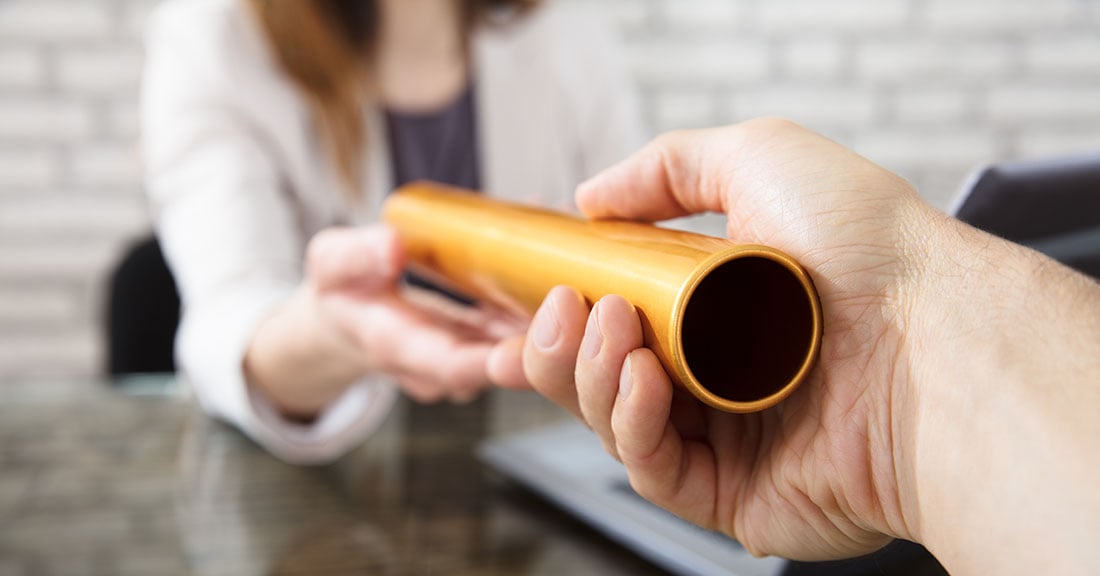 Close up of two people passing a relay baton across a desk in an office setting