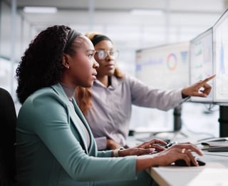 Two woman working together in font of an array of computer monitors.