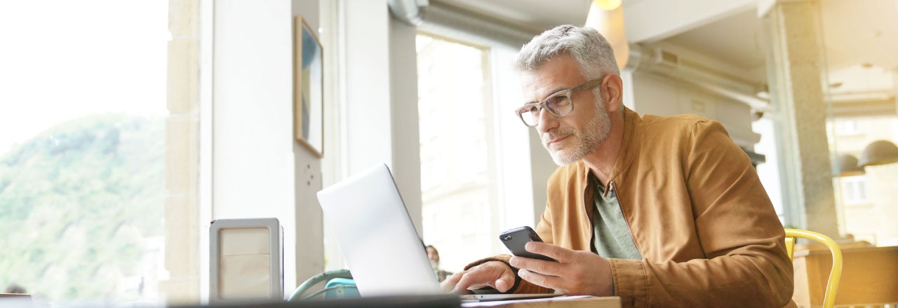 older man looking at a laptop and mobile phone