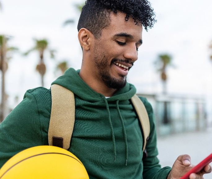 Man in green sweatshrit holding a phone and basketball smiling