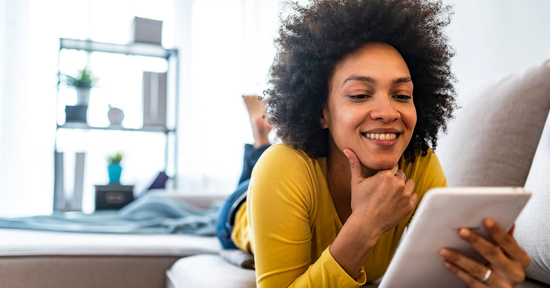 A smiling college student sits on a couch holding and reviewing a student loan debt letter containing her personalized student loan summary from Attigo.