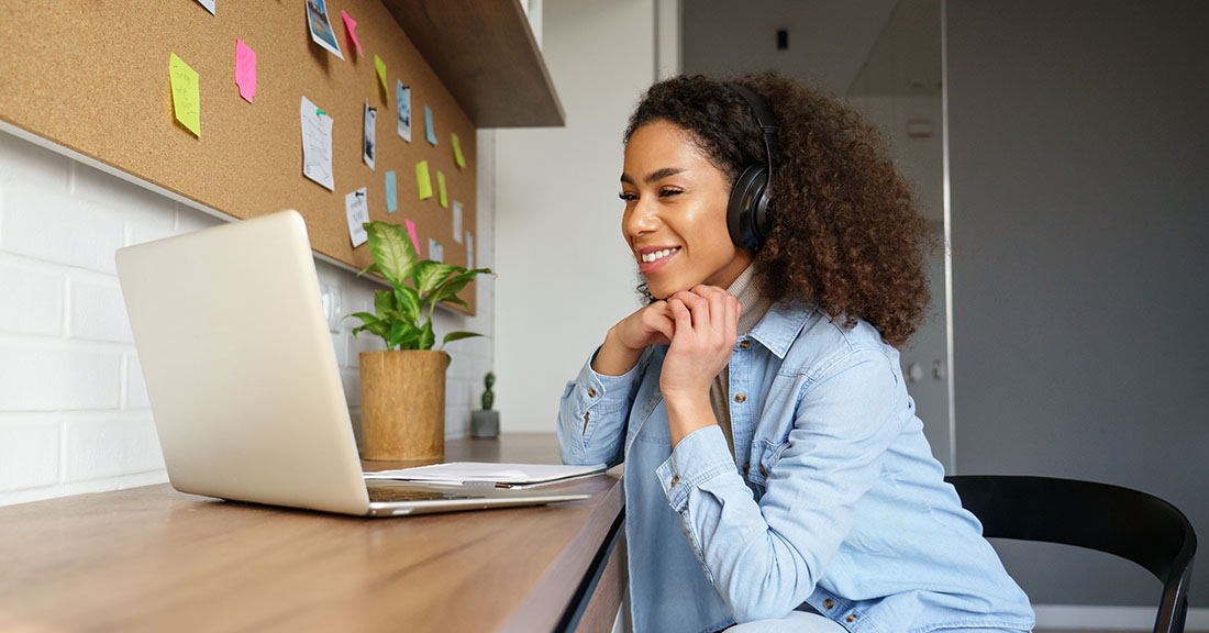 Happy young woman in a casual office setting seated at a desk viewing helpful Attigo resources on her laptop.