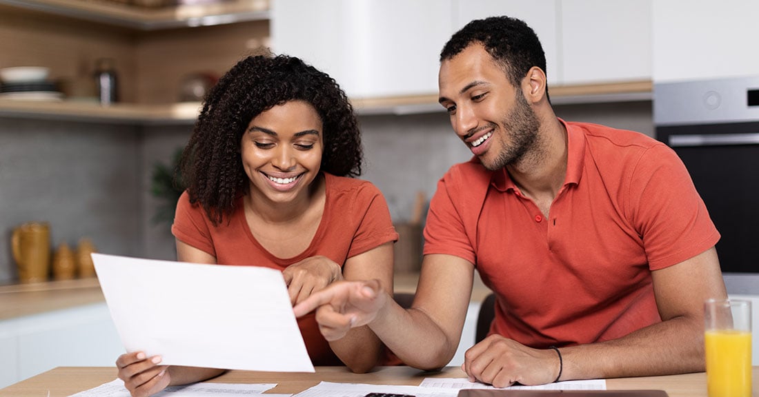 A woman and a man happily reviewing student loan forgiveness information in their kitchen while making plans for the future.